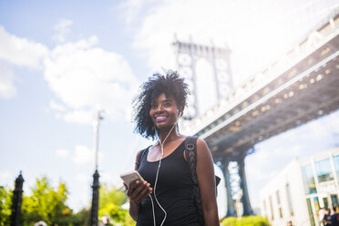 USA, New York City, Brooklyn, lächelnde Frau, die auf der Manhattan Bridge Musik hört - GIOF03083