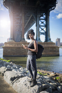 USA, New York City, Brooklyn, lächelnde Frau beim Musikhören unter der Manhattan Bridge - GIOF03087