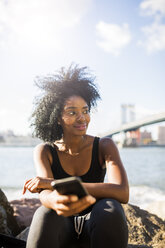 USA, New York City, Brooklyn, lächelnde Frau mit Mobiltelefon am Wasser sitzend - GIOF03100