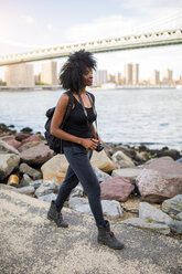 USA, New York City, Brooklyn, woman with camera walking at the waterfront - GIOF03104