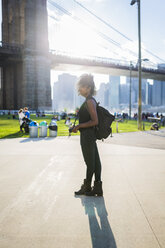 USA, New York City, Brooklyn, woman with camera standing at Brooklyn Bridge - GIOF03110