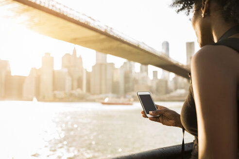 USA, New York City, Brooklyn, Frau mit Mobiltelefon am Wasser - GIOF03114