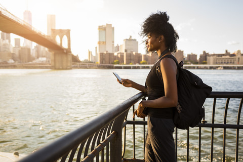 USA, New York City, Brooklyn, woman with cell phone standing at the waterfront stock photo