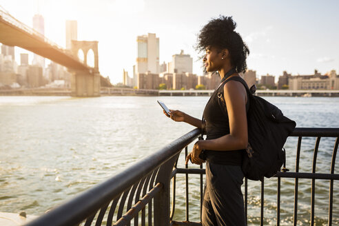 USA, New York City, Brooklyn, woman with cell phone standing at the waterfront - GIOF03115