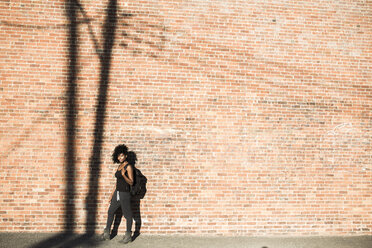 Frau mit Rucksack vor einer Backsteinmauer mit Schatten eines Strommastes - GIOF03116