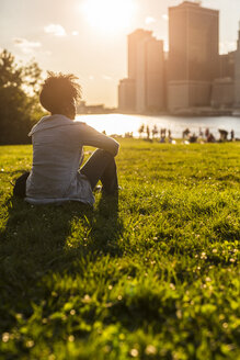 USA, New York City, Brooklyn, Frau sitzt auf einer Wiese und schaut auf die Skyline - GIOF03117