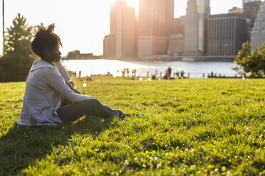 USA, New York City, Brooklyn, woman sitting on meadow looking at the skyline - GIOF03118