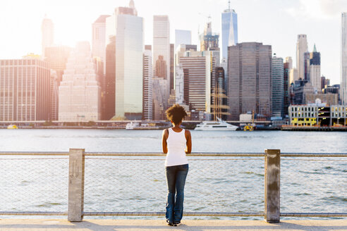 USA, New York City, Brooklyn, woman standing at the waterfront looking at the skyline - GIOF03128