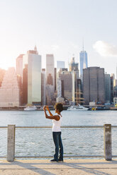 USA, New York City, Brooklyn, woman standing at the waterfront taking cell phone picture - GIOF03130