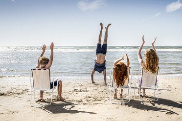 Netherlands, Zandvoort, family clapping hands for father doing a handstand on the beach - FMKF04315