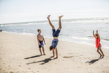 Netherlands, Zandvoort, father with two children doing a handstand on the beach - FMKF04320