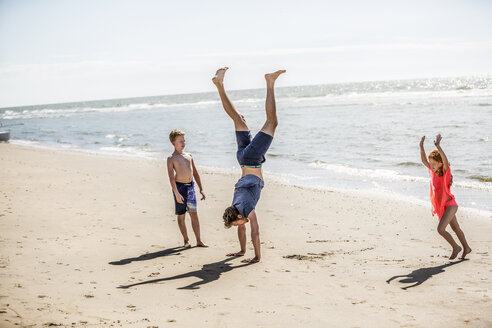 Niederlande, Zandvoort, Vater mit zwei Kindern macht einen Handstand am Strand - FMKF04320