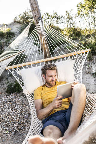 Mann in Hängematte liegend mit Tablet, lizenzfreies Stockfoto