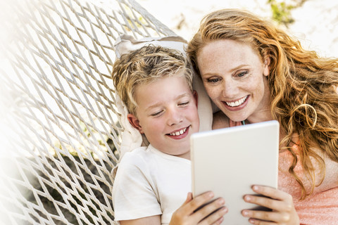 Happy mother and son lying in hammock looking at tablet stock photo