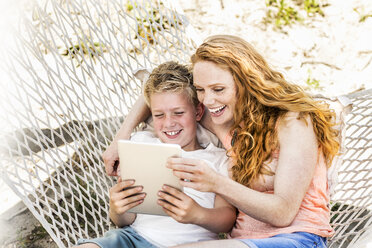 Glückliche Mutter und Sohn in der Hängematte mit Blick auf das Tablet - FMKF04333