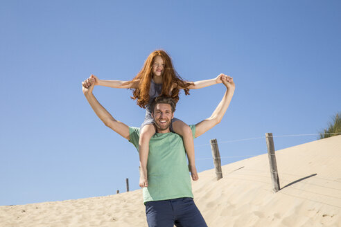 Niederlande, Zandvoort, glücklicher Vater trägt Tochter auf den Schultern am Strand - FMKF04341