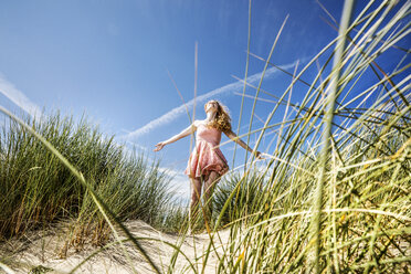 Netherlands, Zandvoort, happy woman standing in dunes with outstretched arms - FMKF04352