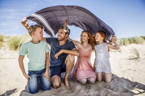 Netherlands, Zandvoort, happy family under a blanket on the beach stock photo