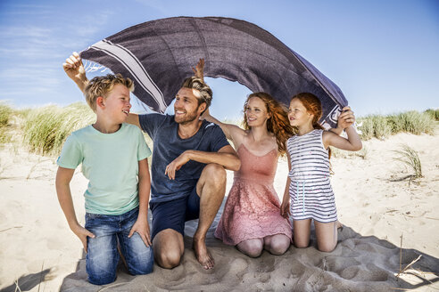 Niederlande, Zandvoort, glückliche Familie unter einer Decke am Strand - FMKF04358