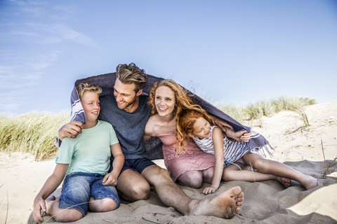 Niederlande, Zandvoort, glückliche Familie unter einer Decke am Strand, lizenzfreies Stockfoto