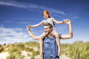 Netherlands, Zandvoort, father carrying daughter on shoulders in beach dunes - FMKF04364
