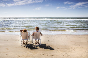 Niederlande, Zandvoort, Junge und Mädchen sitzen auf Stühlen am Strand - FMKF04369