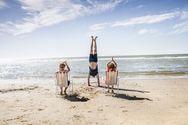 Niederlande, Zandvoort, Kinder klatschen in die Hände, weil ihr Vater am Strand einen Handstand macht - FMKF04374