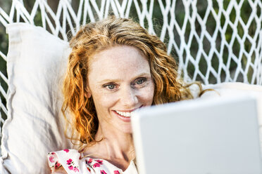 Lächelnde Frau in Hängematte liegend mit Tablet - FMKF04380