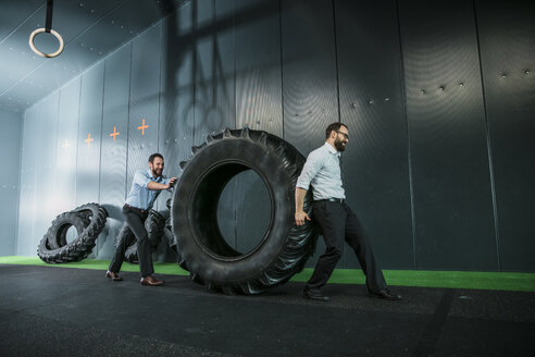 Two businessmen pushing and pulling truck tire - JOSF01339