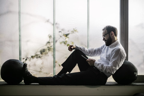 Geschäftsmann sitzt auf der Fensterbank und liest Textnachrichten, lizenzfreies Stockfoto