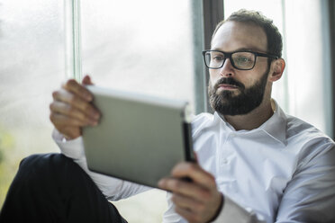 Businessman sitting by window, using digital tablet - JOSF01342