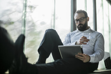 Businessman sitting by window, using digital tablet - JOSF01343