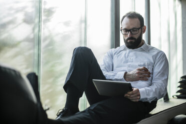 Businessman sitting by window, using digital tablet - JOSF01344