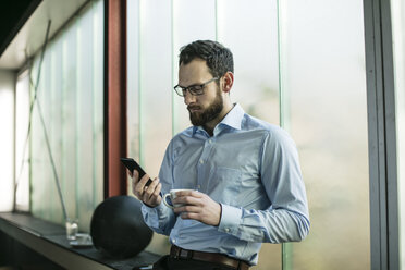 Beschäftigter Geschäftsmann im Büro mit Smartphone - JOSF01351