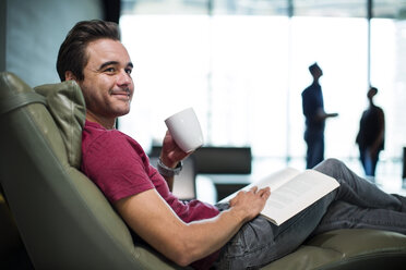 Man in office sitting in armchair, reading a book - ZEF14337