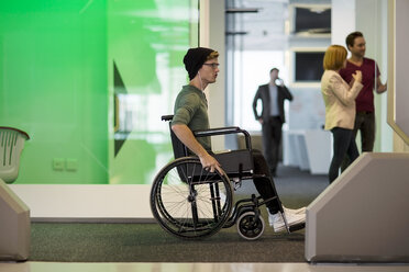 Young man in wheelchair listening to music in office - ZEF14346