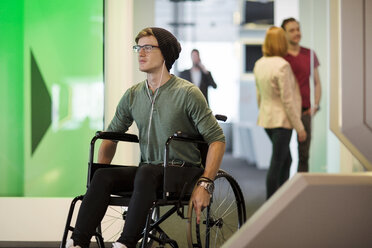 Young man in wheelchair listening to music in office - ZEF14347