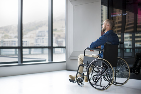 Man in wheelchair looking out of window in office stock photo