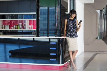 Businesswoman standing in futuristic office, using smartphone - ZEF14396