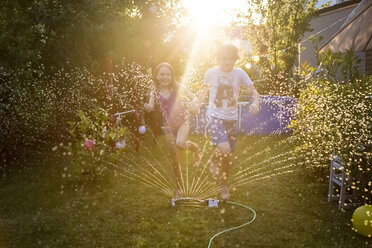 Bruder und Schwester haben Spaß mit dem Rasensprenger im Garten - SARF03348