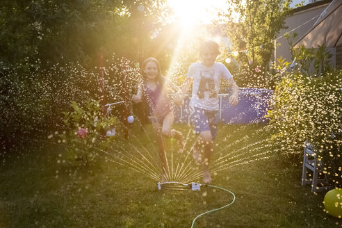 Bruder und Schwester haben Spaß mit dem Rasensprenger im Garten - SARF03348