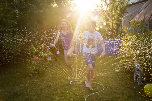 Bruder und Schwester haben Spaß mit dem Rasensprenger im Garten - SARF03349