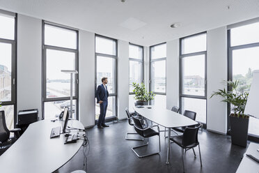 Businessman standing in his office looking out of the window - DIGF02676