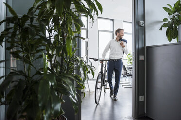 Lächelnder Geschäftsmann mit Fahrrad im Büro - DIGF02679