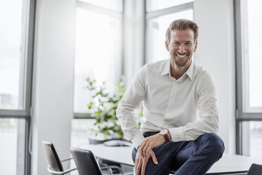 Porträt eines lachenden Geschäftsmannes, der auf einem Besprechungstisch im Büro sitzt - DIGF02698