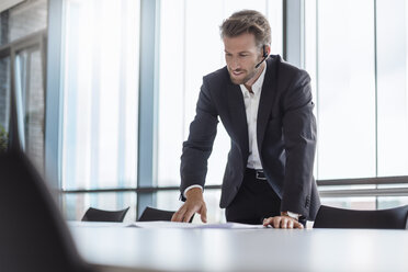 Businessman with bluetooth headset standing in conference room explaning - DIGF02706