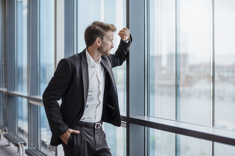 Geschäftsmann steht im Büro und schaut aus dem Fenster, lizenzfreies Stockfoto