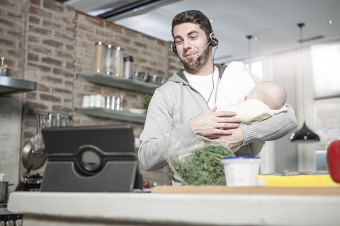Vater mit Headset und Tablet in der Küche mit Baby, lizenzfreies Stockfoto