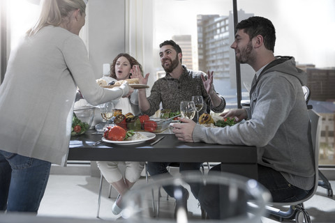 Woman serving food to surprised friends at dinner table stock photo