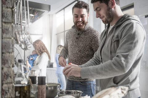 Zwei Männer mit Familie bei der Zubereitung einer Mahlzeit in der Küche, lizenzfreies Stockfoto